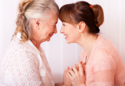 caregiver and elder woman smiling while placing their foreheads closer with each other